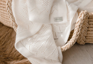 Heirloom baby blanket draped over a babies bassinet. Shows lace detail in classic white knitted merino wool. Made in New Zealand by Wilderling. 